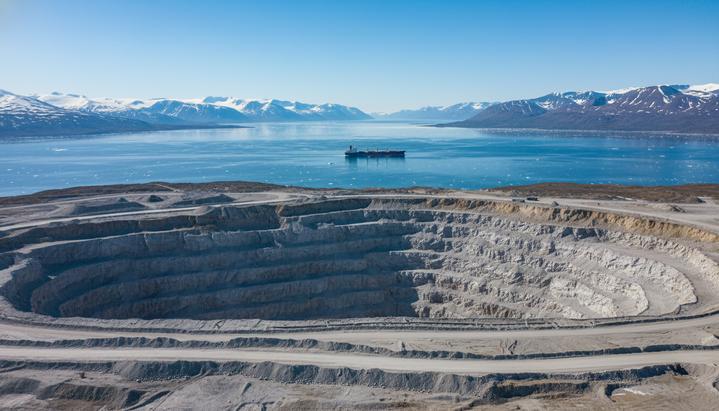 Открытая разработка месторождения анортозита на скалистом побережье Гренландии, на фоне фьорда с грузовым судном.